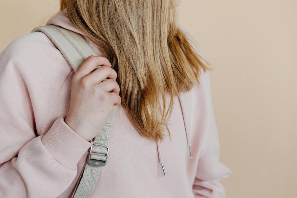 pexels-photo-8147450-8147450 Close-up of a teenage girl holding a backpack strap in a pink hoodie. Studio setting.
